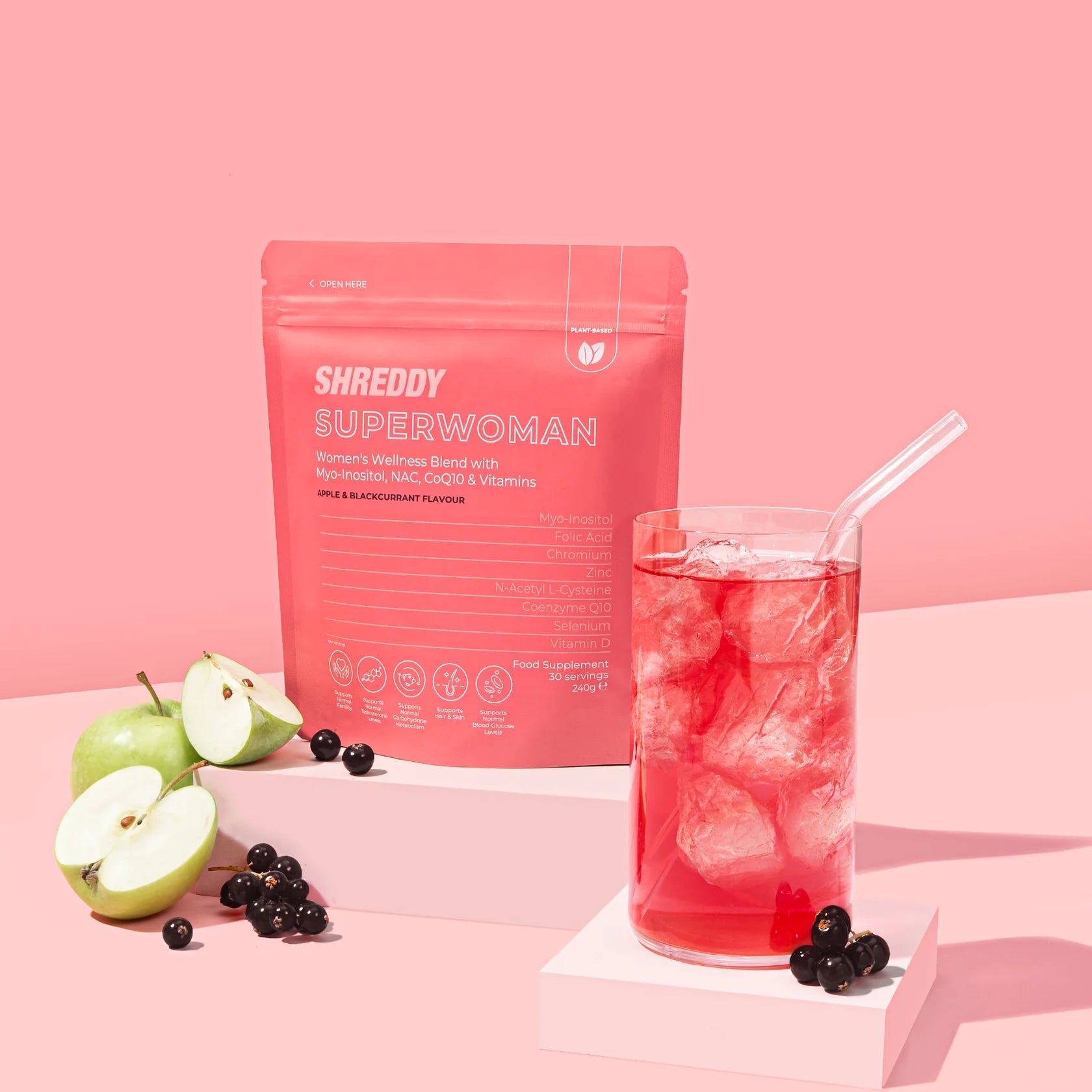 Shreddy Superwoman supplement package with a glass of red drink and apples on a pink background